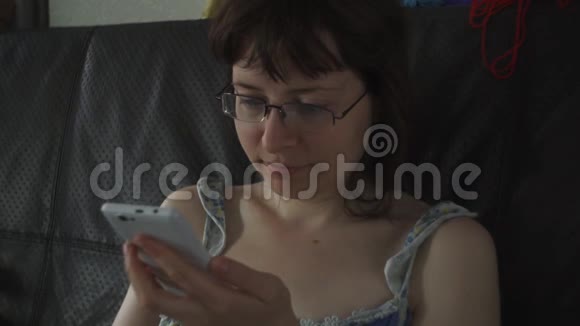 一个戴着眼镜和睡衣的女人坐在黑色沙发上用手机视频的预览图