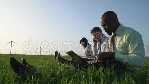 一群穿着西装的人在风电场附近的草地上工作阳光明媚视频的预览图