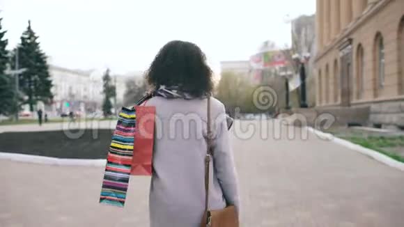 多莉拍摄的迷人的混合种族女孩转身与购物袋和微笑成相机年轻女子走路视频的预览图