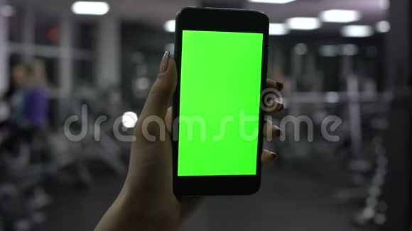 女性手持智能手机在健身房绿色屏幕在线健身应用视频的预览图