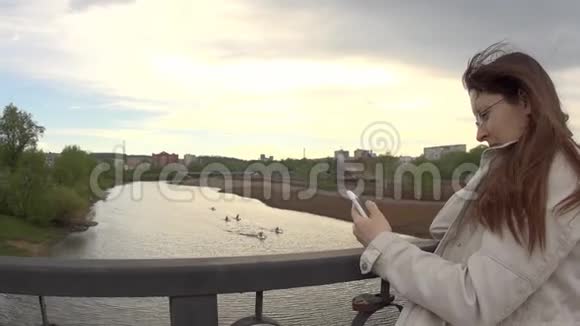 一个穿白夹克的年轻女子在城市桥上用电话视频的预览图