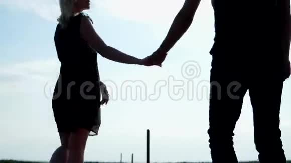 浪漫的年轻夫妇剪影女人和男人在黎明牵手阳光的照耀视频的预览图