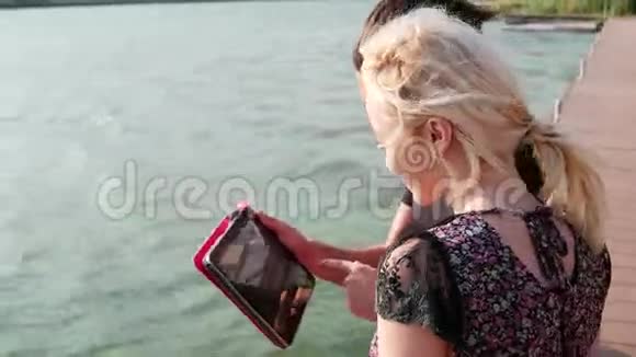 年轻人花时间在ipad上看电影男孩和女孩在湖边使用平板电脑视频的预览图