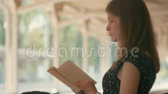 千禧一代女士正在阅读一本坐在长凳上等待假期火车的书视频的预览图