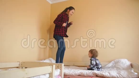 欢快的笑着蹒跚学步的男孩看着姐姐在床上跳跃视频的预览图