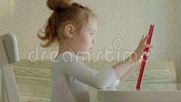 可爱的小女孩坐在厨房或桌子旁的房间里用平板电脑玩上网冲浪视频的预览图