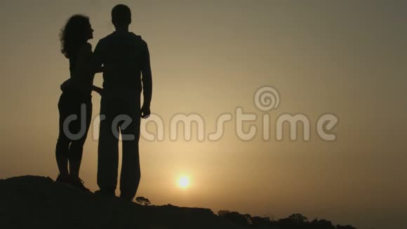 幸福的一对相爱的情侣拥抱着笑着欣赏着山上的日落视频的预览图