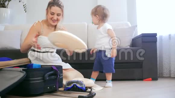 4k视频母亲带着蹒跚学步的儿子在手提箱里收拾东西视频的预览图