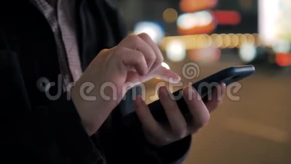 男人在抽象模糊的街头夜晚使用智能手机背景夜间城市汽车灯光关闭电话视频的预览图