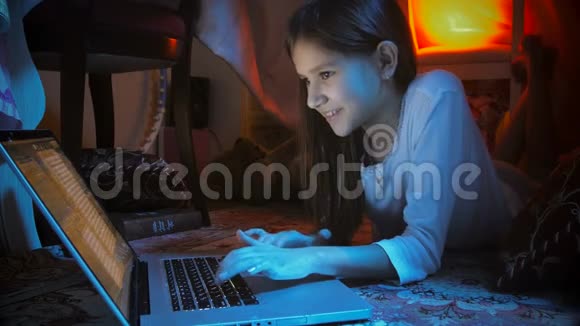 穿睡衣的可爱的微笑女孩晚上在帐篷里用笔记本电脑视频的预览图