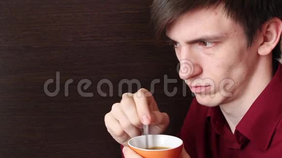 一个手里拿着一个橙色杯子的年轻人搅动了一茶匙看着一边不高兴视频的预览图