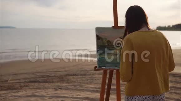年轻的艺术家画一把调色板刀仍然生活在女孩靠近大海或河流的地方视频的预览图