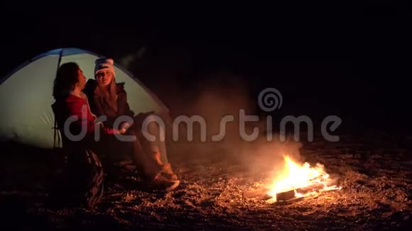 一对年轻夫妇坐在火炉旁在海边用帐篷露营春天视频的预览图