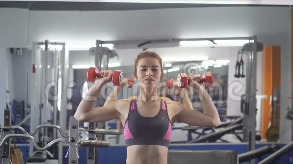 年轻漂亮的运动女孩用哑铃做压肩运动在运动健身房锻炼视频的预览图