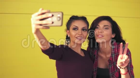 两个迷人的女人在自拍和显示和平标志时摆姿势漂亮女孩用智能手机拍照视频的预览图