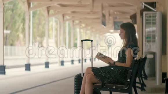 年轻女子正在看书坐在车站的长凳上等火车视频的预览图