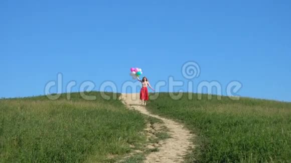 绿色草地上快乐奔跑的女孩带着五颜六色的气球视频的预览图