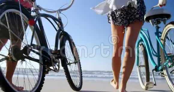 阳光明媚的一天一对夫妇骑着自行车在海滩上散步视频的预览图