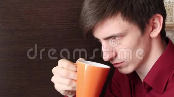 一个年轻人把一个橘子杯子端到嘴里小口地喝了一口视频的预览图