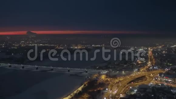 空中无人驾驶飞机观看雪河边覆盖交通堵塞的夜间城市视频的预览图