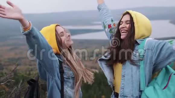 两个年轻快乐的女人在美丽的山顶上跳舞举起手臂越过夕阳的天空视频的预览图