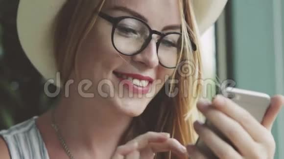 女孩在手机上和朋友聊天女人在咖啡馆的智能手机上写按摩微笑视频的预览图