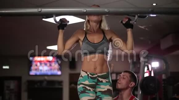 健身房里的一个女人在教练的帮助下收紧横杆视频的预览图
