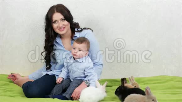 年轻的妈妈和儿子坐在绿色的草地上快乐的妈妈和孩子坐在草地上复活节兔子视频的预览图