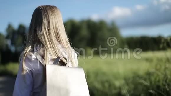 一个漂亮的金发小女孩在穿过田野的沙地上上学视频的预览图