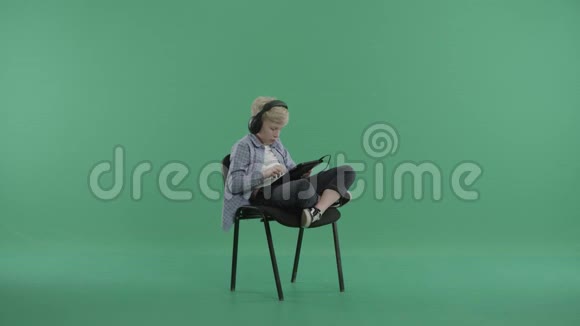 男孩坐在椅子上戴着耳机在平板电脑上听音乐视频的预览图