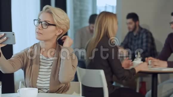 时尚年轻女性戴眼镜坐在咖啡馆里用智能手机自拍的肖像视频的预览图