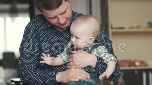 年轻的父亲把他的小儿子抱在怀里一个1岁的孩子坐在他父亲腿上幸福的家庭视频的预览图