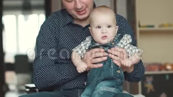 年轻的父亲把他的小儿子抱在怀里一个1岁的孩子坐在他父亲腿上幸福的家庭视频的预览图