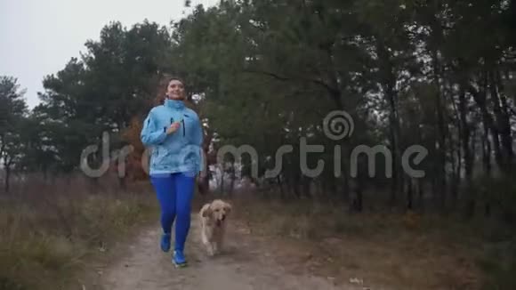 在秋天的森林里带着狗慢跑的健壮的女人视频的预览图