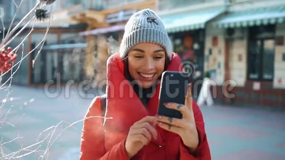 穿着灰色帽子和红色外套的女孩在阳光明媚的冬日站在街上通过Skype视频聊天视频的预览图