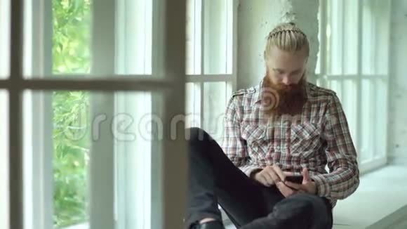悲伤的长胡子男人用智能手机在家的窗台上发短信视频的预览图