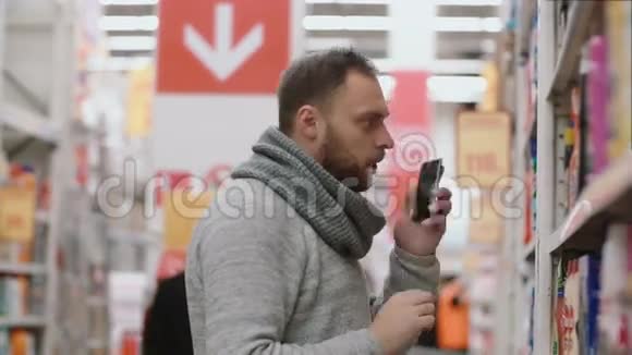 年轻人站在超市货架前拿着电话打电话取项目并征求意见4K视频的预览图