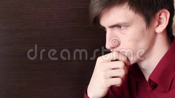 一个穿红色衬衫的年轻人用下巴抚摸他的手仔细看着视频的预览图