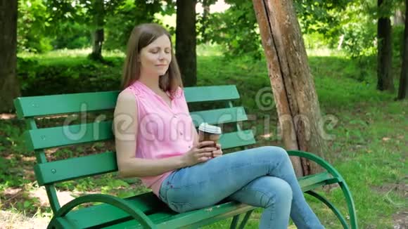漂亮的女孩坐在公园的长凳上喝咖啡可爱的女孩喝咖啡在露天放松视频的预览图