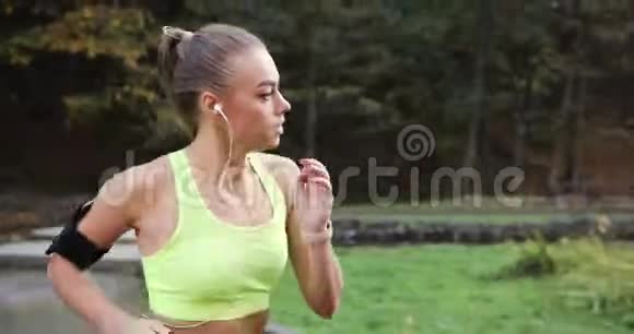 公园里的女跑步者穿着五颜六色慢跑服的女人听音乐沿着公园的小路跑视频的预览图