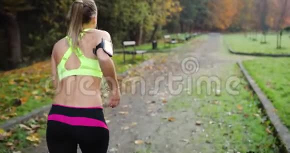 公园里的女跑步者穿着五颜六色慢跑服的女人听音乐沿着公园的小路跑视频的预览图