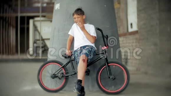 男孩坐在BMX自行车上和热狗一起吃东西视频的预览图