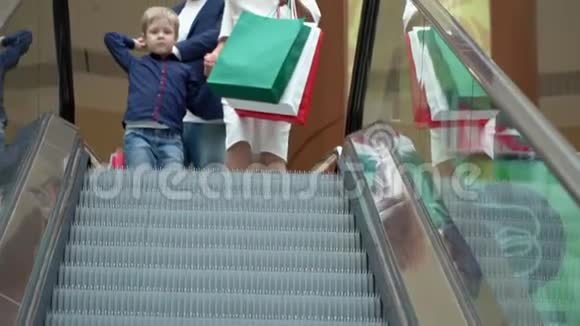 这对年轻夫妇带着一包礼物爬上扶梯度假购物中心自动扶梯上的情侣视频的预览图