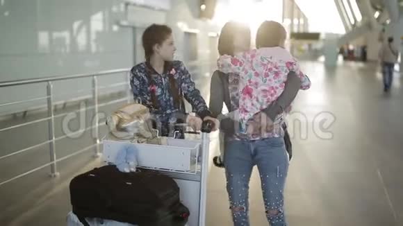 一个女人带着两个女儿沿着机场大厅拉着行李手推车和袋子等候区的乘客视频的预览图