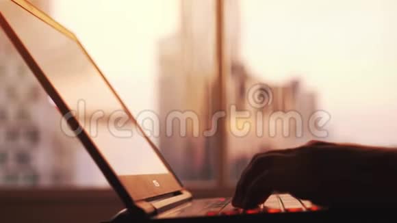 在日落时分商人的手型在城市建筑的大窗户旁的笔记本电脑上工作3840x2160视频的预览图