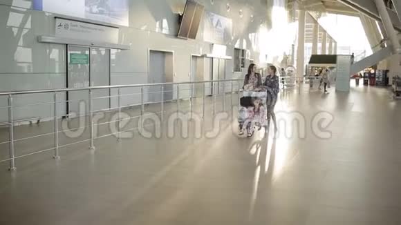 女人带着两个女儿沿着机场大厅拉着行李手推车和袋子等候区的乘客视频的预览图