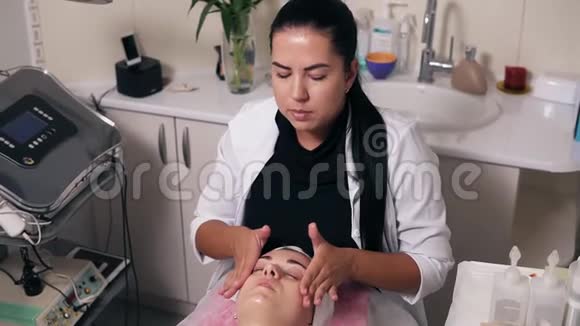 女性美容师正在水疗沙龙做面部按摩年轻女子闭着眼睛躺在沙发上视频的预览图