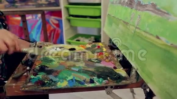 女艺术家把油画颜料混合在调色板上在画室里画一幅风景画视频的预览图