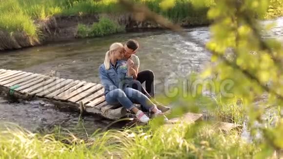年轻夫妇坐在河边的桥上拥抱视频的预览图