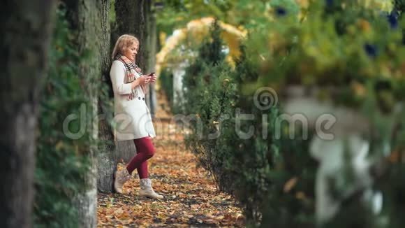 秋天公园里微笑的女人在手机上打字视频的预览图